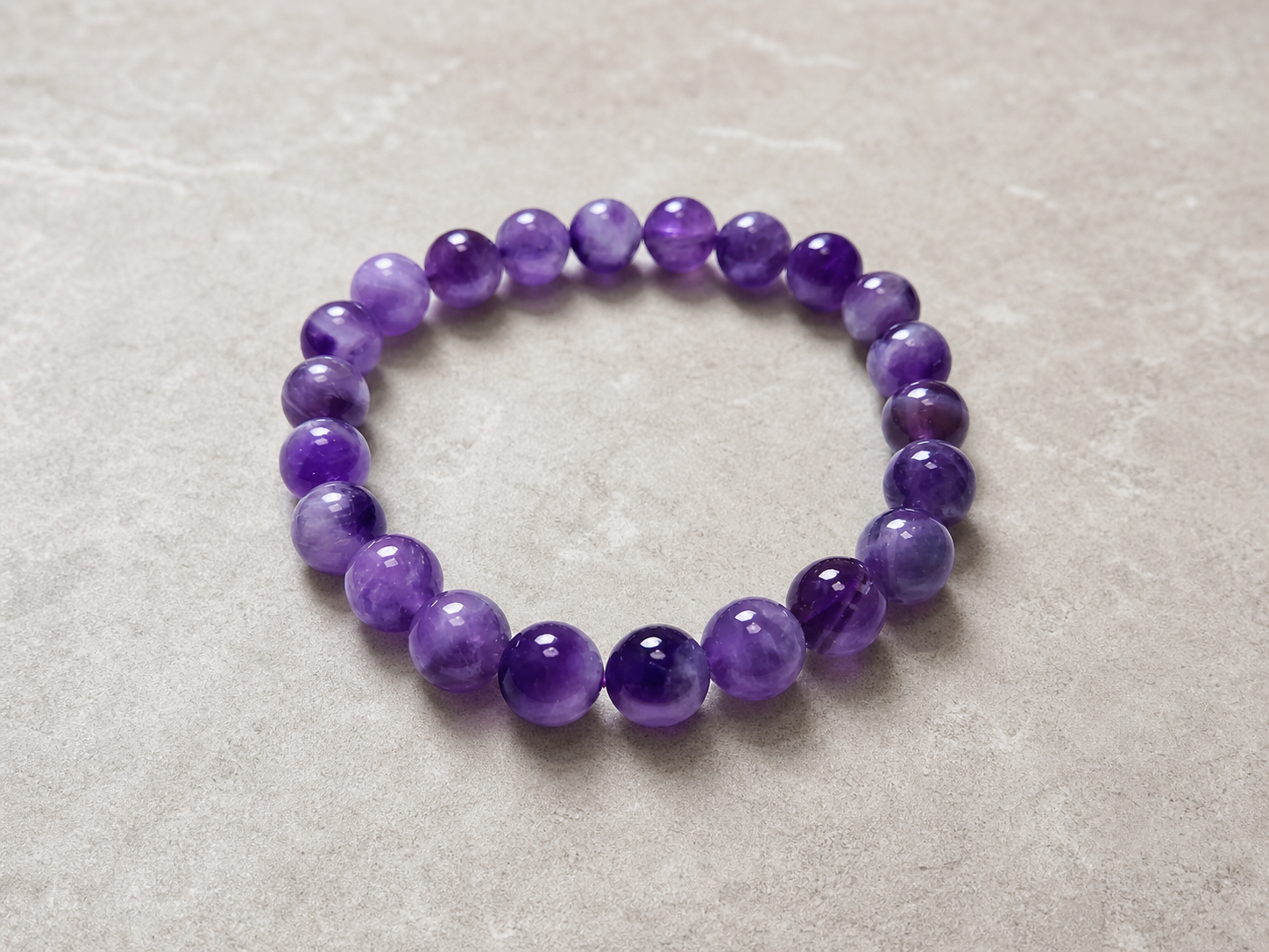 Amethyst bracelet for women with purple beads on a neutral stone surface.