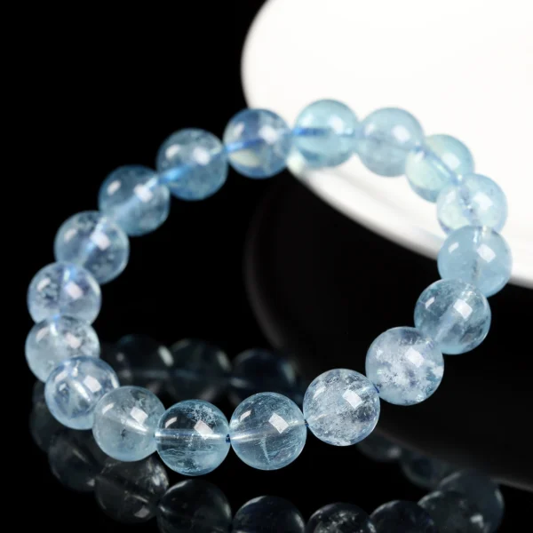 Single-strand aquamarine bead bracelet beside a white display stand